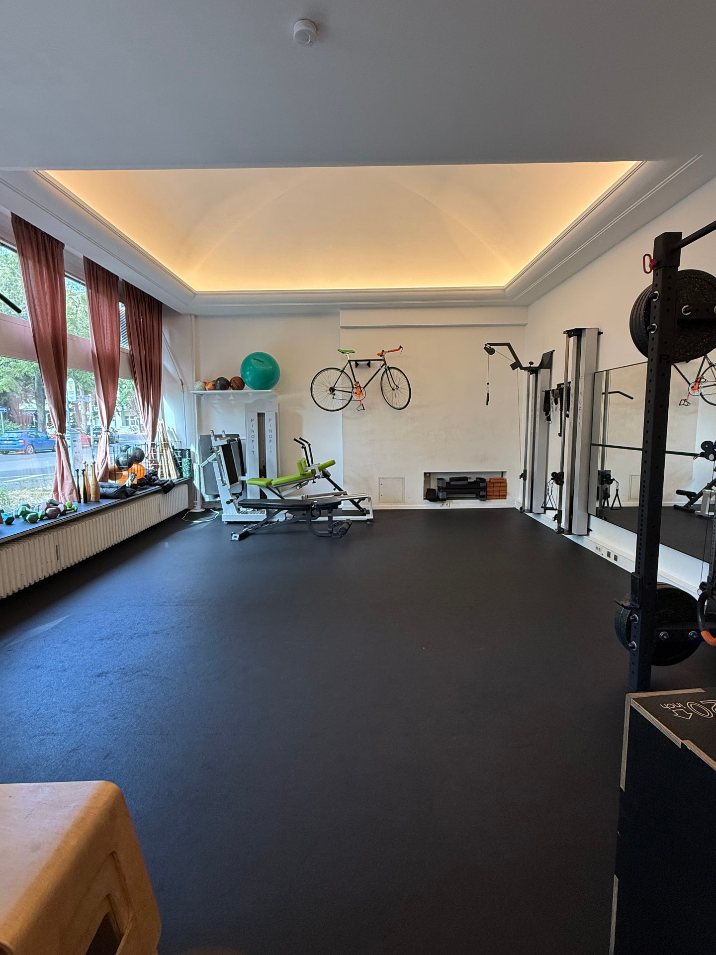 Heller Trainingsraum von Fit durch Physio in Berlin-Schöneberg mit Kabelzug, Rack, Trainingsbänken und Kleingeräten für gerätegestützte Physiotherapie.