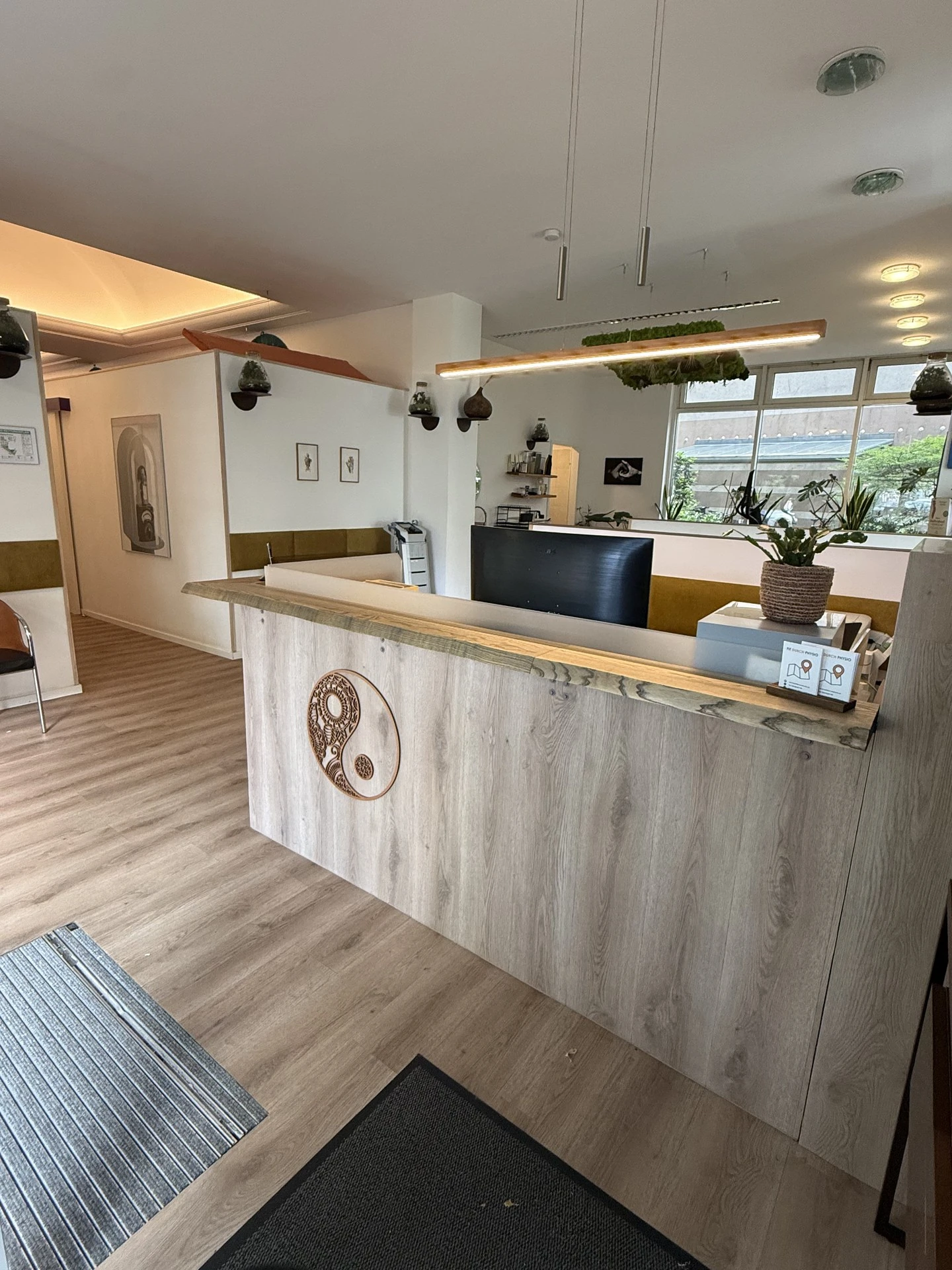 Empfangsbereich von Fit durch Physio mit Holztheke, Zimmerpflanzen und warmer Beleuchtung